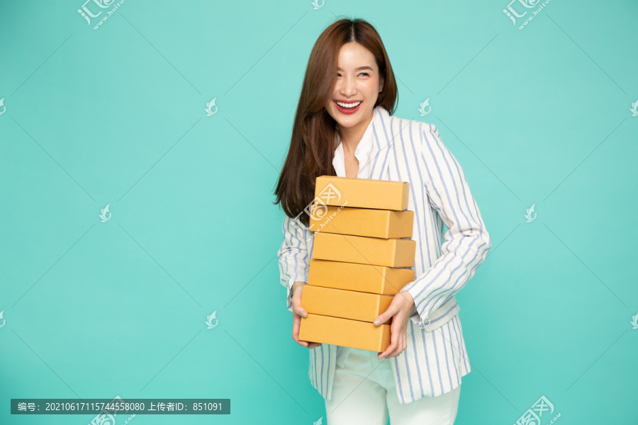 快乐的亚洲女人微笑着拿着包裹盒，包裹盒在浅绿色背景上隔离开来，传递快递和运输服务理念