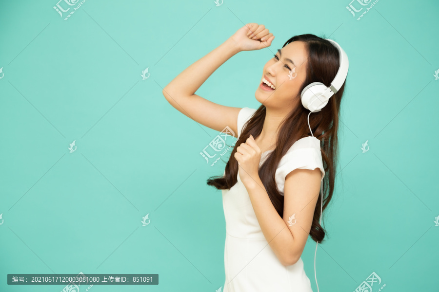 在绿色背景上隔离的智能手机上，年轻的亚洲美女戴着耳机在播放列表歌曲应用程序中跳舞和听音乐