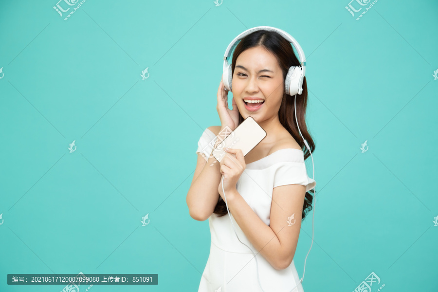 在绿色背景上隔离的智能手机上，年轻的亚洲美女用耳机收听播放列表歌曲应用程序中的音乐