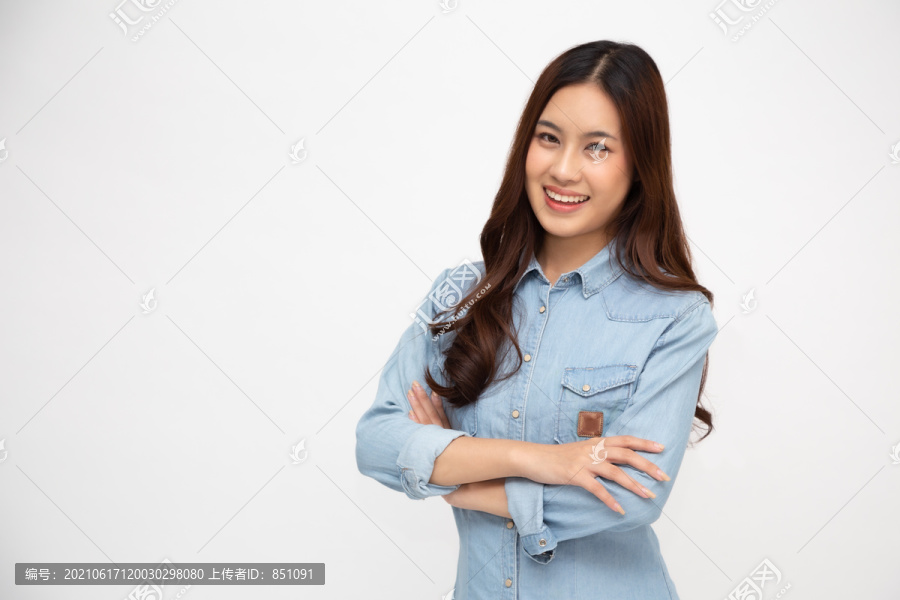 亚洲女性的肖像，穿着蓝色牛仔衬衫，双臂交叉，微笑隔离在白色背景上，年轻女性微笑着看着相机，快乐的感觉