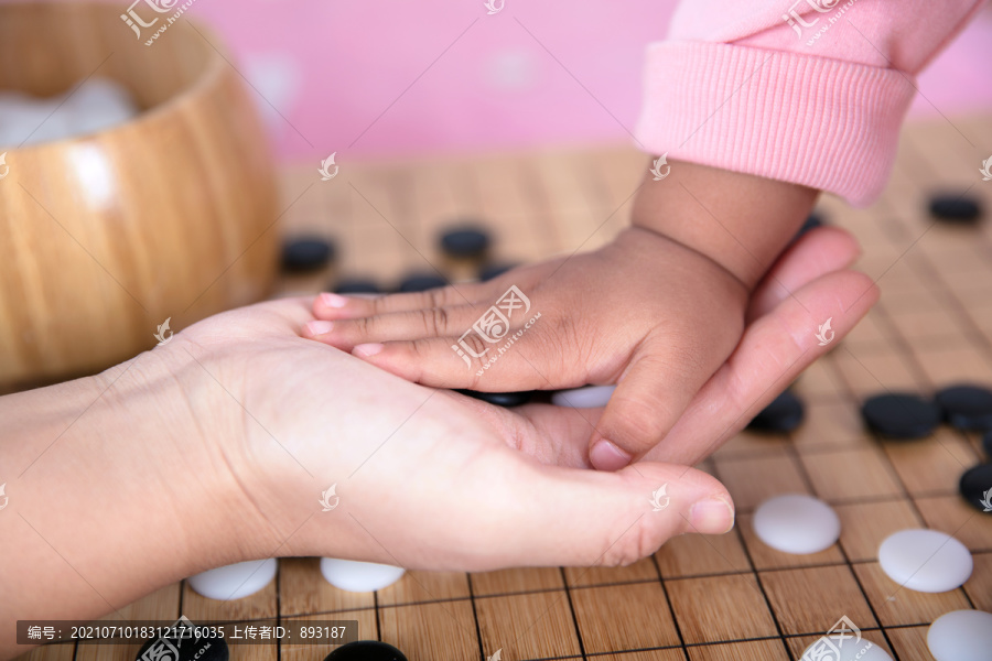 围棋棋盘前成年人的手和孩子的手