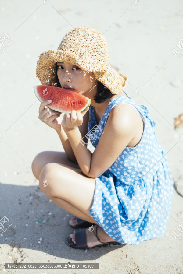 可爱的黑发女孩坐在沙滩上吃着红西瓜。
