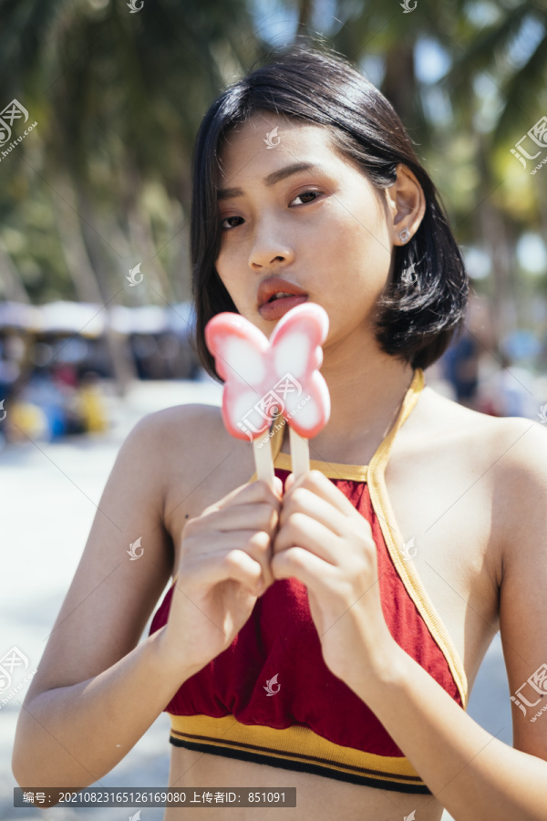 穿着红色上衣的性感女孩站着拿着粉色蝴蝶冰淇淋。