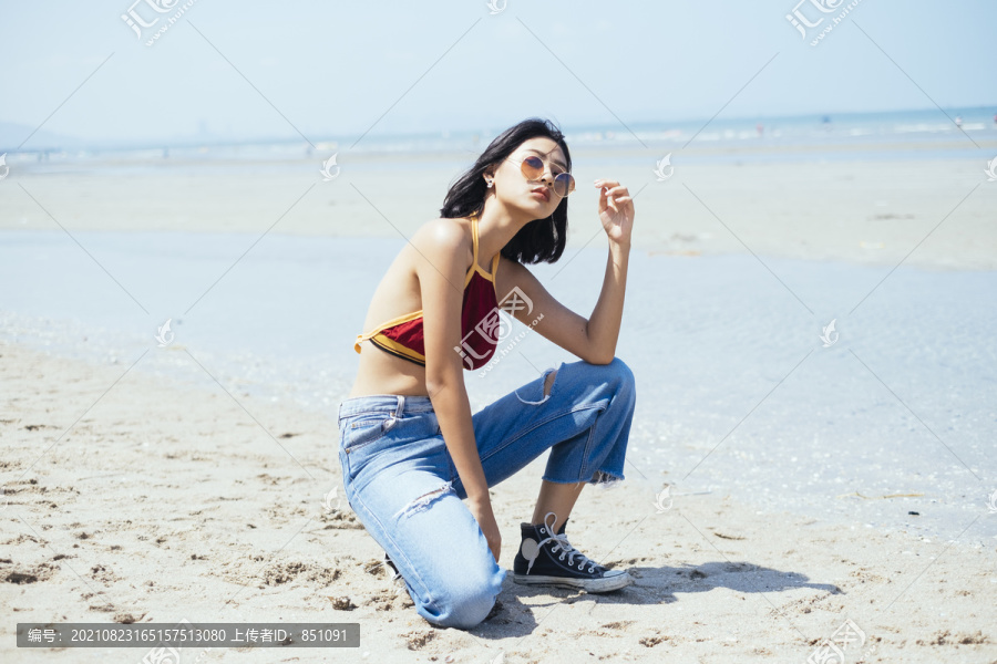 穿着红色短上衣的性感女孩以别致的姿势坐在海滩上。