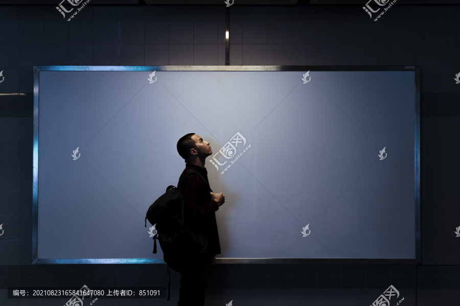 光秃秃的男人背着背包站在白板前，在一个灯光下，剪影。