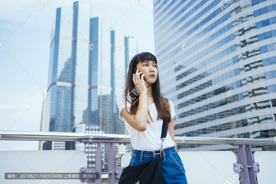 在城市里，一位留着刘海发型的可爱泰国年轻女子在手机上聊天。