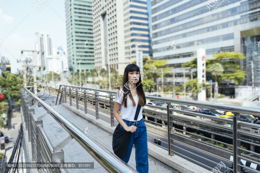 穿着白色衬衫和蓝色牛仔裤的旅行者年轻女子自信地走在天桥上。