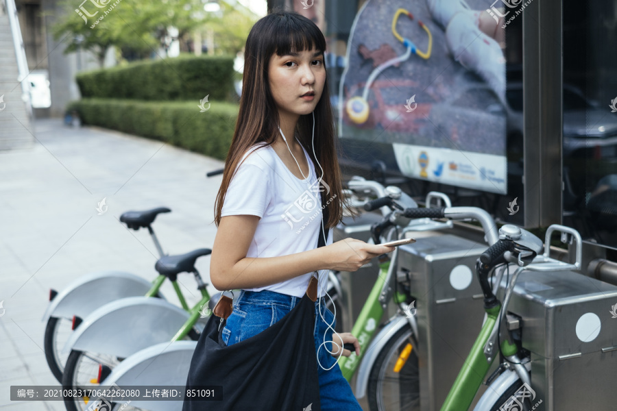 一名年轻的泰国女子戴着耳机听音乐，试图在人行道上骑自行车。