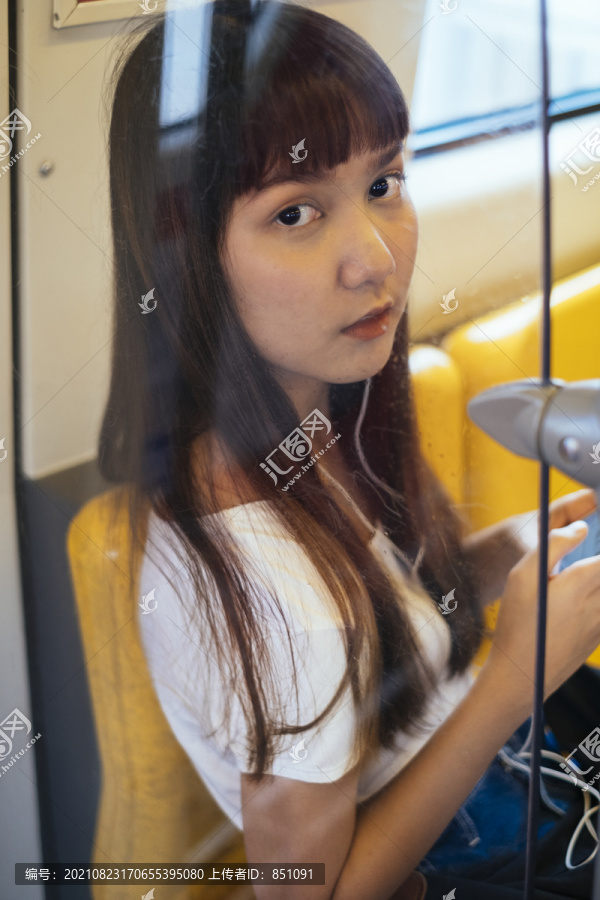 坐在火车上，在玻璃窗后面留着刘海发型的可爱泰国女人。