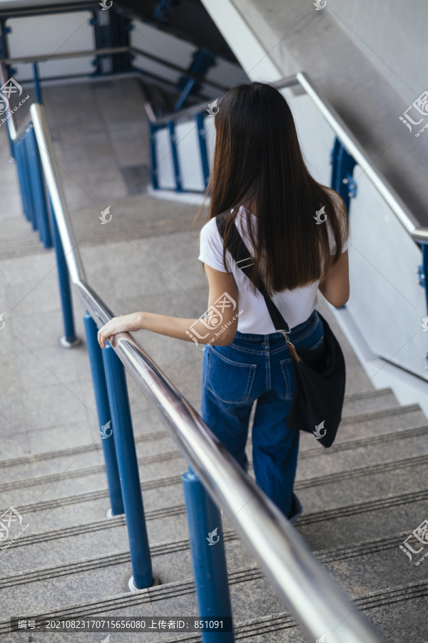 一位身穿白色衬衫和蓝色牛仔裤的匿名年轻女子走下楼梯。