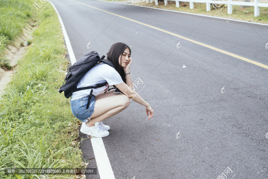 年轻的亚裔泰国长黑发女旅行者在路上等车。搭便车的人。