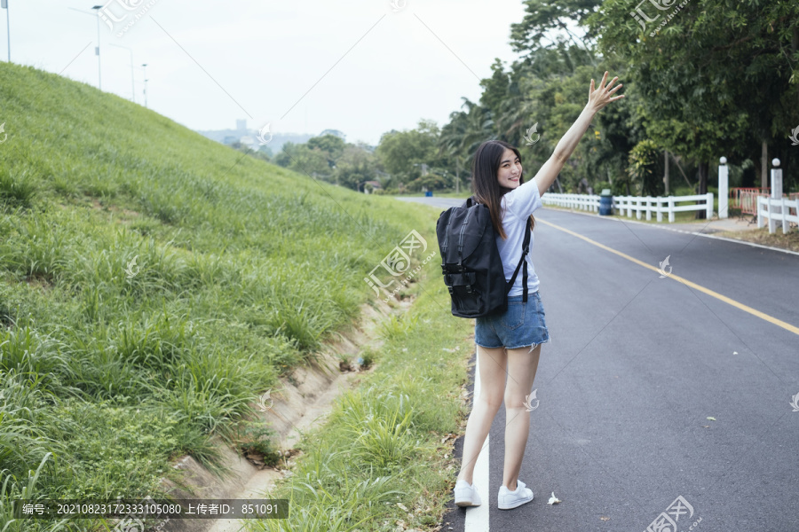 年轻的亚裔泰国人，长着深色头发的女旅行者，在路上搭便车。