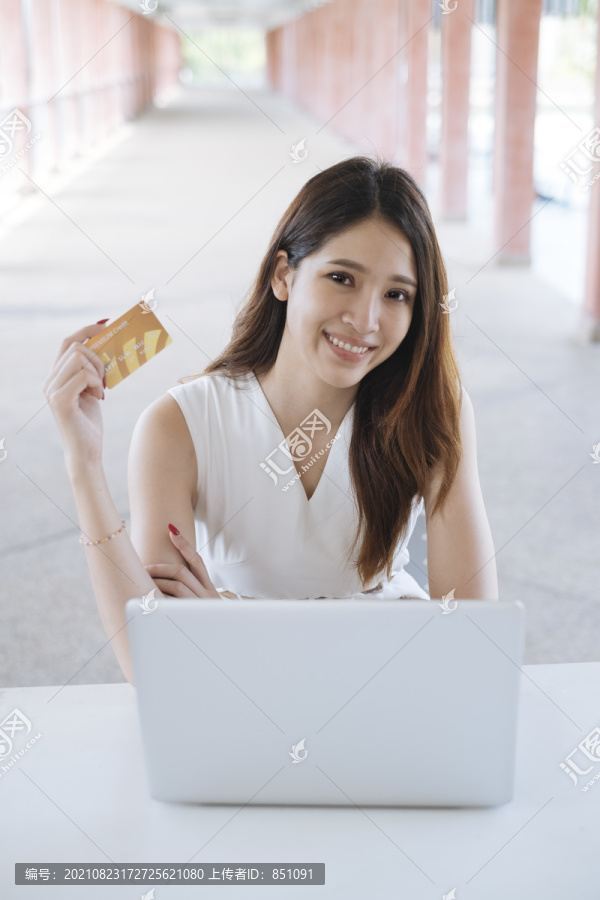 年轻漂亮的亚洲女士用笔记本电脑上的信用卡进行网上购物。