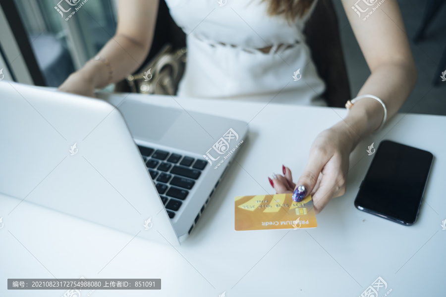 网上购物概念-美丽的女人拿着信用卡，用它做网上购物。女孩用笔记本电脑用信用卡购物。