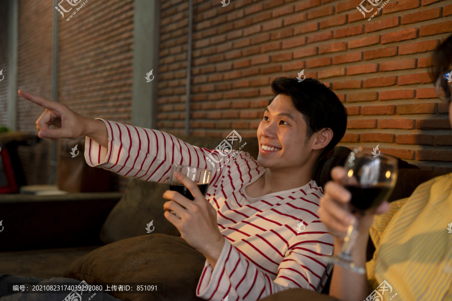 一对亚洲LGBTQ+男性喜欢在家里一起喝酒和看电视。