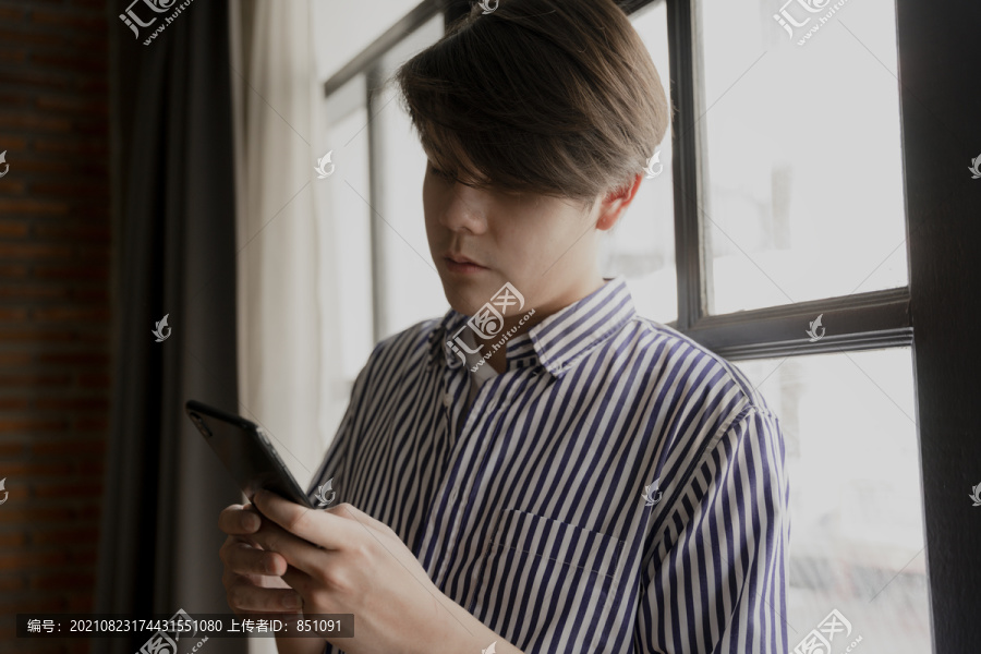 亚洲年轻人在窗口附近使用智能手机。