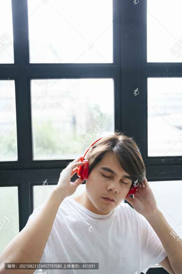 亚洲年轻人闭着眼睛用无线耳机听音乐。