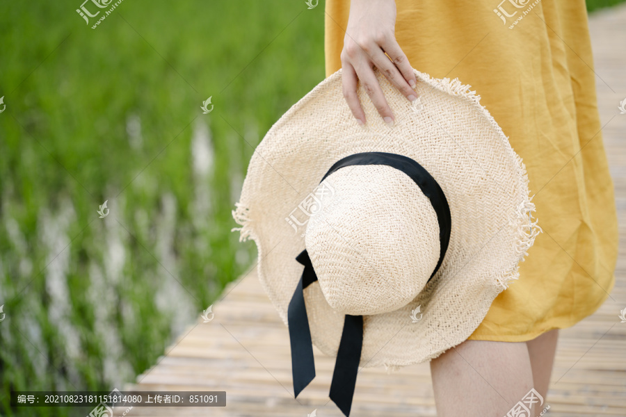 穿着黄色衣服的妇女紧握着草帽走在横跨稻田的木桥上。