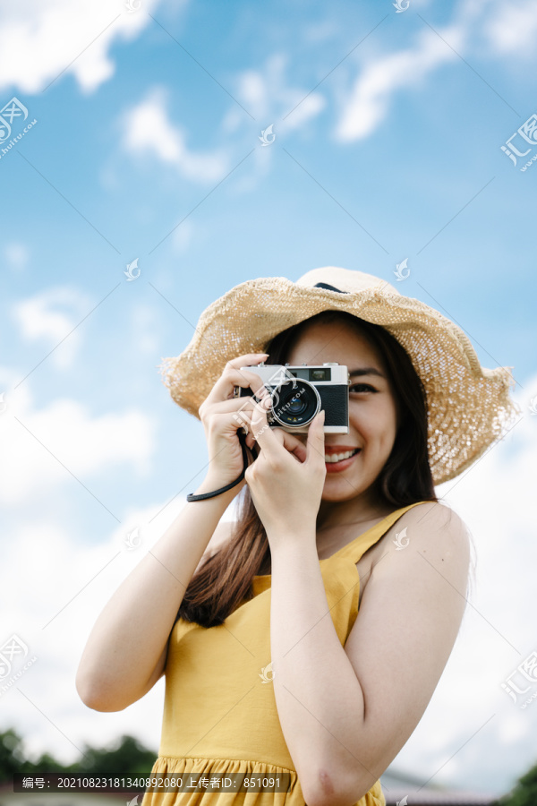 美丽的亚洲女旅行者在明亮的天空背景下用复古胶卷相机拍照。