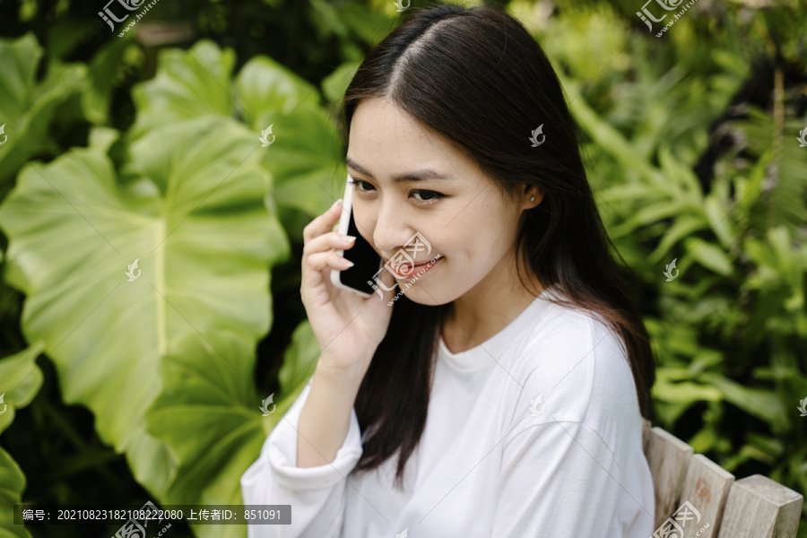 穿着白衬衫的亚洲美女在户外公园打电话。