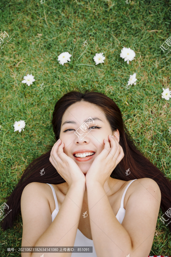 美丽的亚洲旅行家女子躺在草地上，身上开着白花。