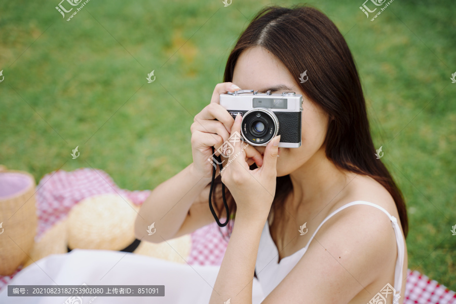 美丽的亚洲女人在公园户外用胶卷相机拍照。