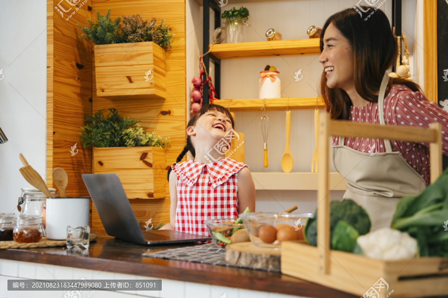 亚洲小孩和妈妈在厨房里互相帮助做饭。人们在网上搜索食物配方。