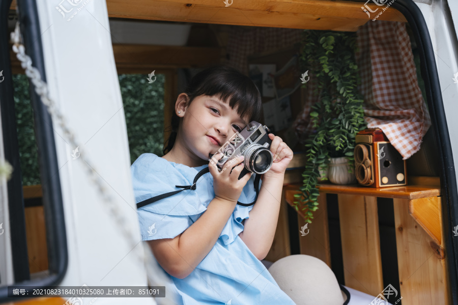漂亮的亚洲小孩在休闲车里拿着复古胶卷相机。