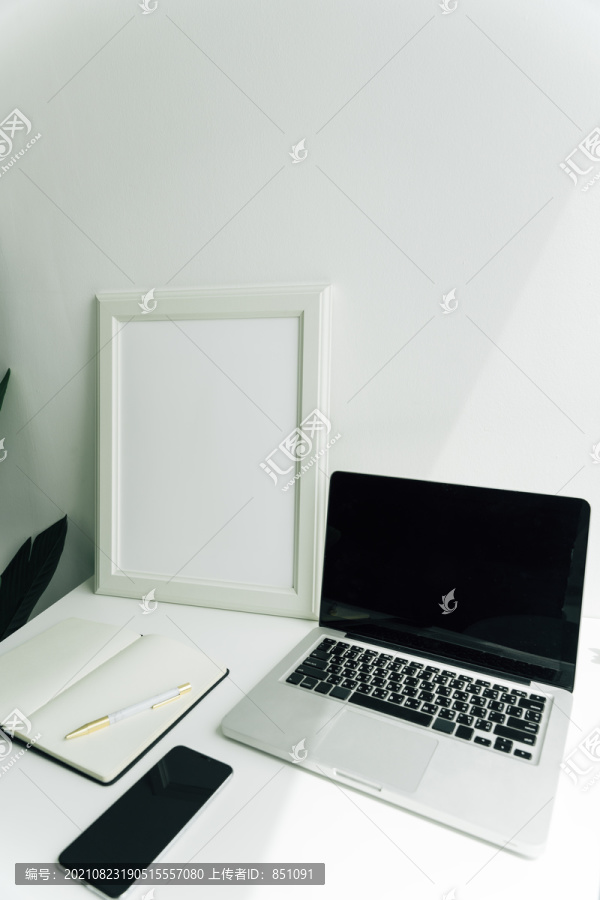 最小的白色房间工作空间，配备黑屏笔记本电脑、书籍和智能手机。
