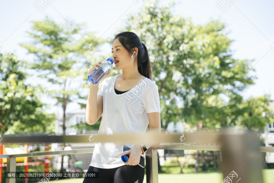 健康的亚洲女性在公园锻炼后饮用瓶装水。