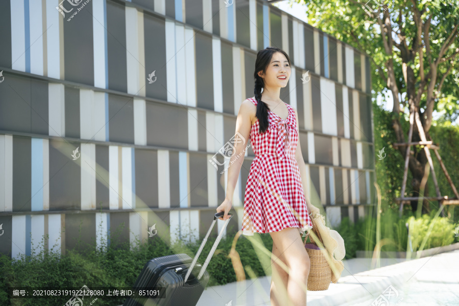 美丽的亚洲年轻女旅行者，穿着粉色连衣裙，带着旅行行李。