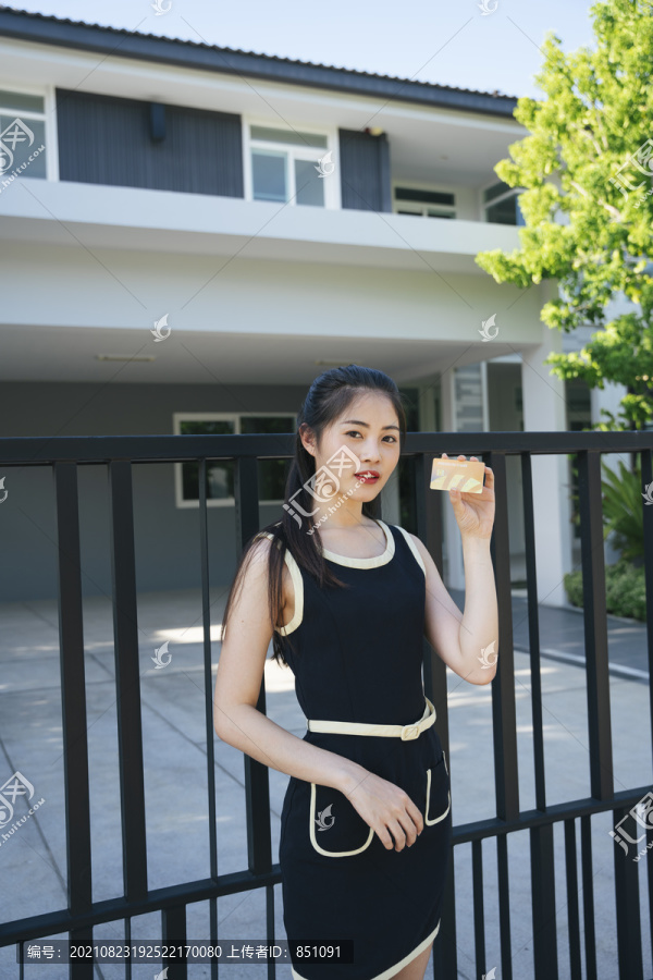 美丽的亚洲女人在豪宅前用信用卡。购买地产的概念。
