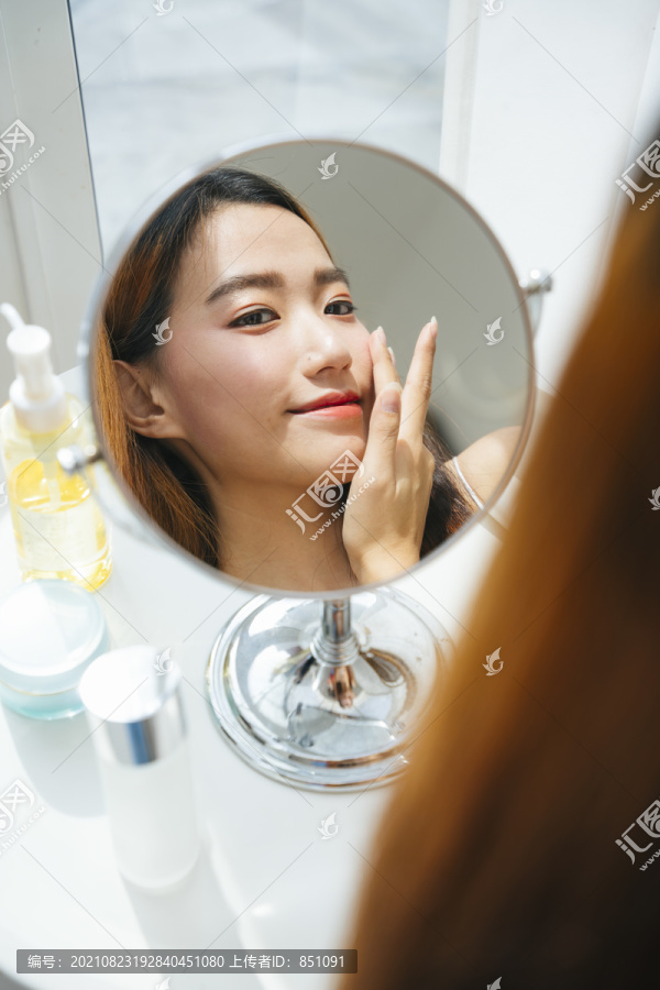 年轻的亚洲女人在镜子前化妆。