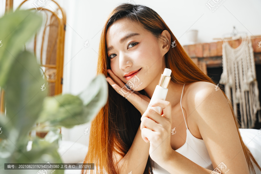 在自然光下拿着润肤霜瓶子的年轻亚洲女性的特写照片。