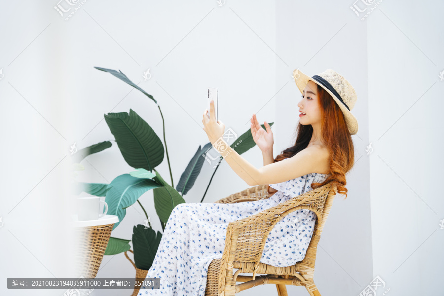 侧视图-美丽的亚洲女旅行者戴着帽子，在椅子上使用智能手机。