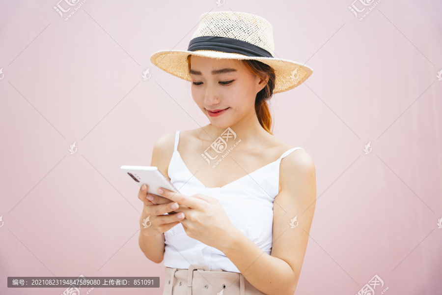 美丽的亚洲女人戴着粉色背景的智能手机帽子。
