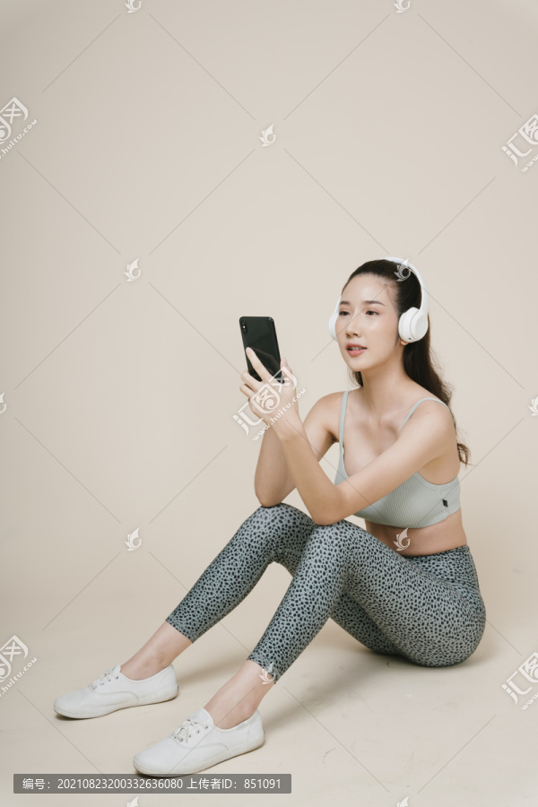 亚洲运动女性运动员的肖像，坐在地板上，用耳机和智能手机听音乐。