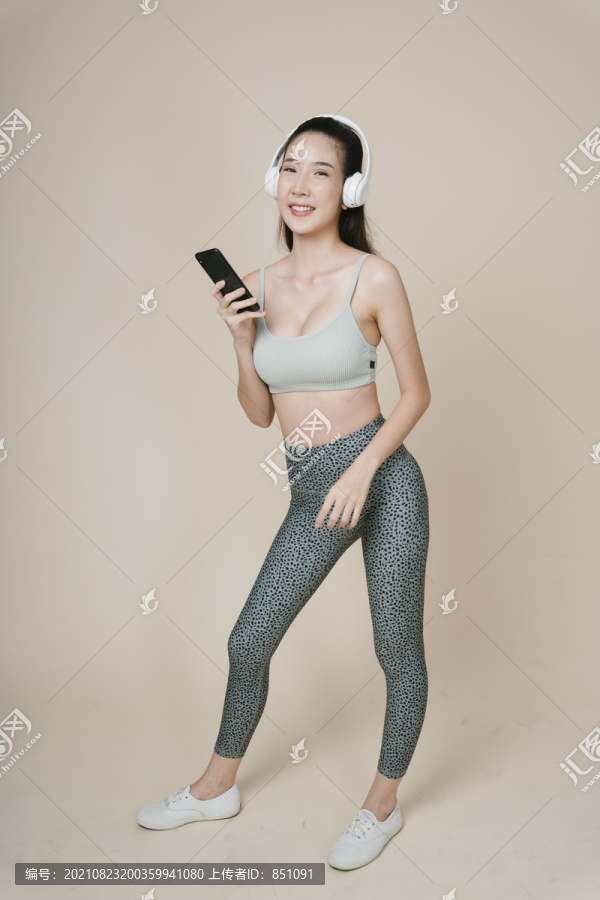 亚洲运动女性运动员肖像，使用智能手机，通过无线耳机收听音乐。
