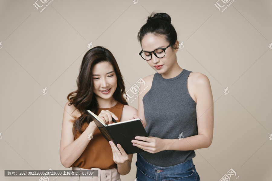 两位穿着休闲衬衫的亚洲女商人看着一本书中的财务报告。