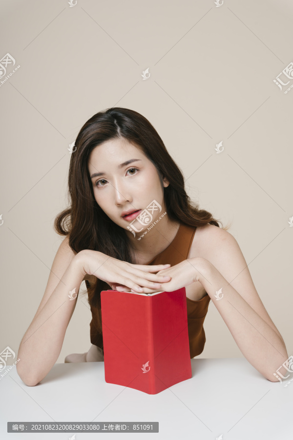 办公桌上拿着一本红皮书的美丽年轻亚洲女人的肖像。