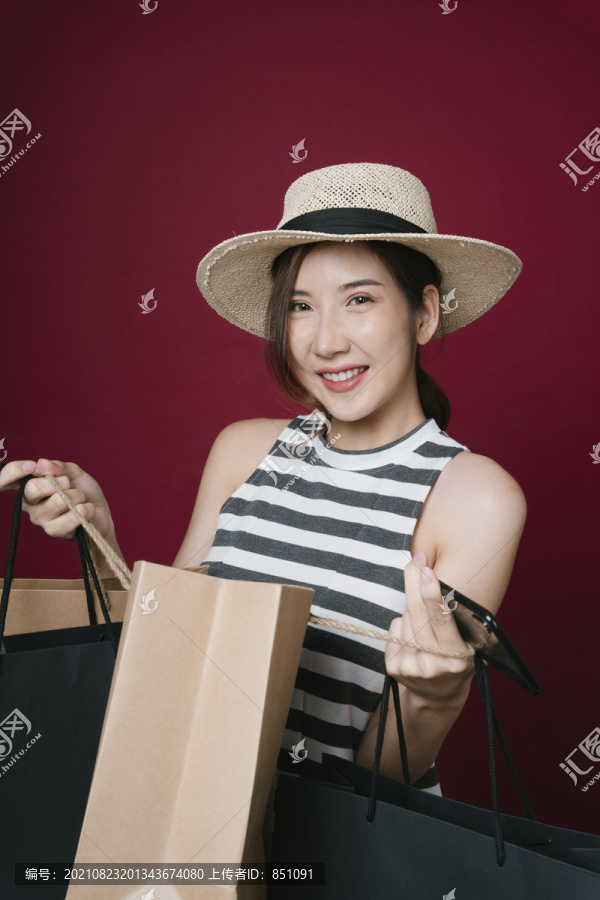 兴奋的美女戴着帽子，手持购物纸袋，在红色背景上隔离的肖像。
