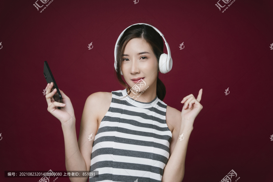 美丽的亚洲年轻女子的画像戴着耳机欣赏音乐。