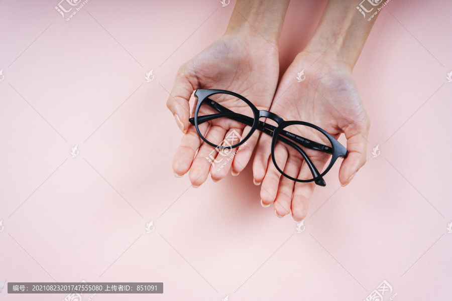 手持眼镜的妇女的手在浅粉色背景上被隔离。