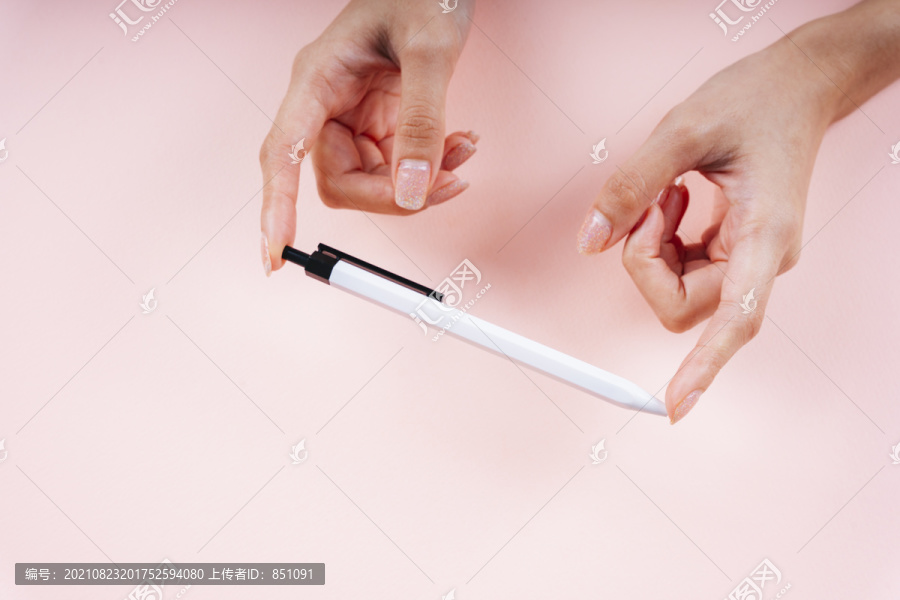 手持白色钢笔的女士的手，淡粉色背景。
