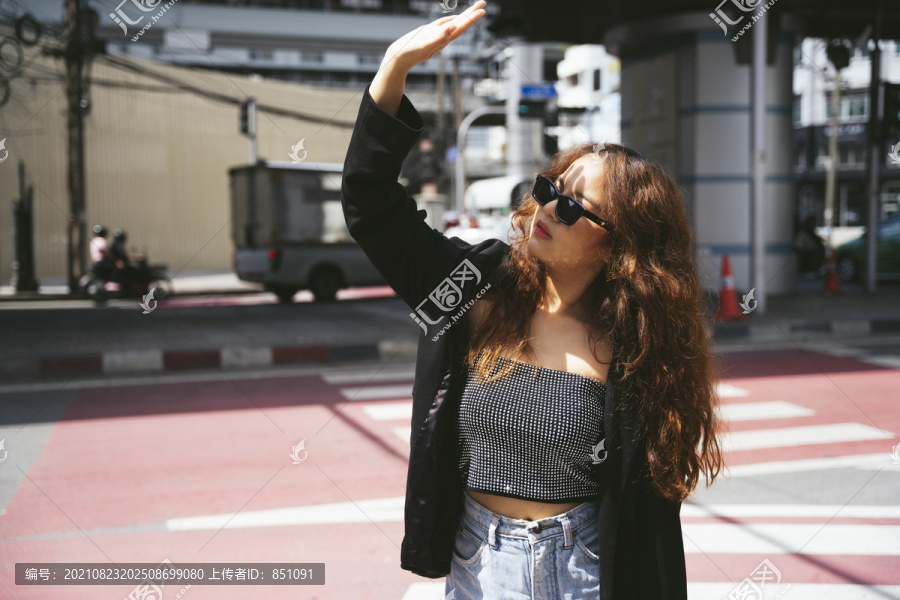 在十字路口，一位年轻的亚洲女性戴着墨镜，穿着黑色夹克，脸上遮住了阳光。