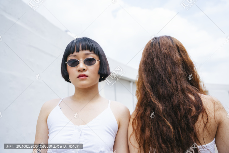 年轻的亚洲女人戴着太阳镜在街上走过另一个女孩的照片。概念。