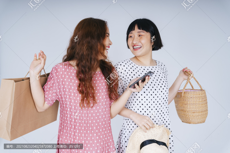 两位年轻的亚洲女性在白色背景下享受智能手机应用程序上的在线购物。