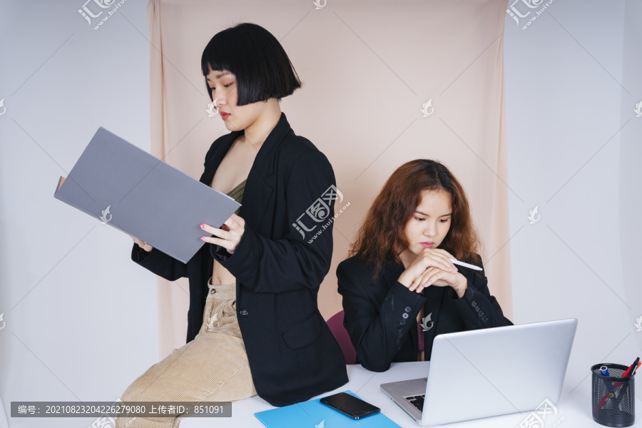 两位穿着正式夹克套装的年轻亚洲商界女性在办公室一起工作的肖像。