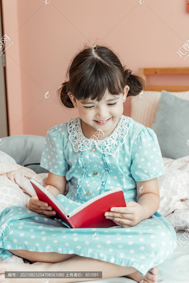 穿着蓝色衣服的快乐女孩在卧室看书。