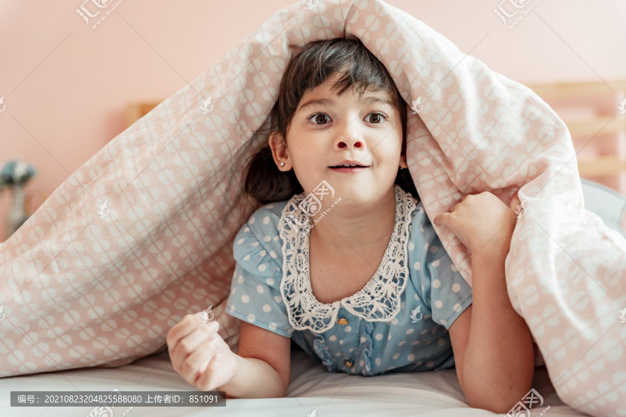 兴奋的小女孩在卧室的毯子下做鬼脸。
